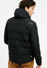 Schwarze gepolsterte Jacke mit Kapuze, die eine glatte Textur und ein Logo auf der Schulter aufweist. Seitentaschen sind vorhanden, die für Wärme ausgelegt sind.