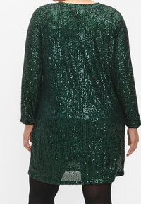 Grön paljettklänning med långa ärmar och lös passform. Baksidan har en rundad halsringning och en hög slits i fållen.