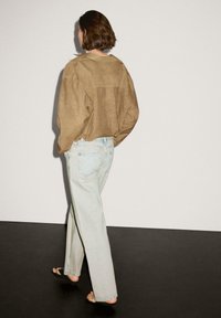 Brunlinne, överdimensionerad skjorta i kombination med ljusblå, raka jeans. Skjortan har en bakre sömdetalj och är stylad med platta sandaler.