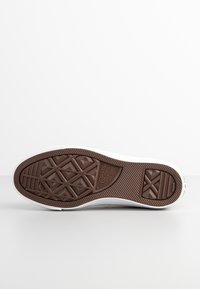 Suola di sneaker bianca con un battistrada in gomma marrone a motivo diamante, caratterizzata da scanalature testurizzate e il logo "Converse All Star" impresso.