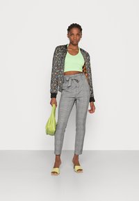 Jaqueta bomber floral, top cropped verde menta, calças de cintura alta xadrez cinza, bolsa verde limão e sandálias amarelas de slide.