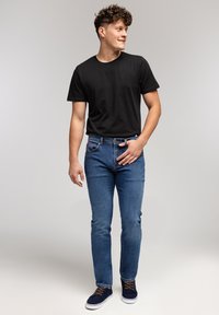 Czarny bawełniany t-shirt, niebieskie dżinsy i granatowe trampki. Dżinsy mają klasyczny krój z prostymi nogawkami oraz subtelnymi detalami w szyciu.