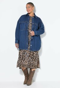 Jeansjacka med avslappnad passform, två bröstfickor och knäppning med knappar, lagd över en klänning i brunt leopardmönster och bruna stövlar.