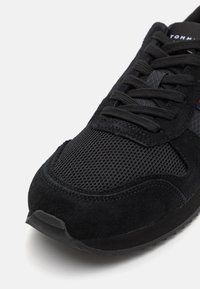 Scarpa da ginnastica nera con un mix di materiali in suede e mesh, superficie testurizzata, suola spessa e lacci neri prominenti.