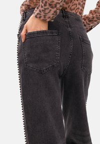Svarta denimjeans med rak passform, med sidoliknande dragkedjor och kontrasterande detaljer. Inkluderar bakfickor och subtila texturdetaljer.