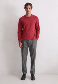 Czerwony sweter z miękkiego dzianego materiału, zestawiony z szarymi plisowanymi spodniami. Czarna para butów dopełnia stylizację, charakteryzująca się prostym, dopasowanym krojem.