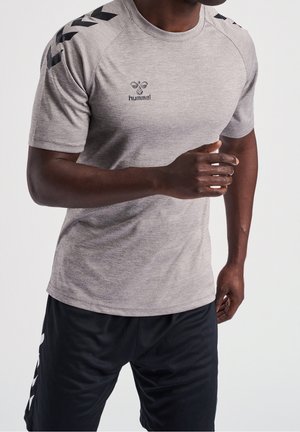 Mand iført grå hummel sportstrøje og sorte shorts, i en løbe- eller joggestilling mod ensfarvet baggrund.
