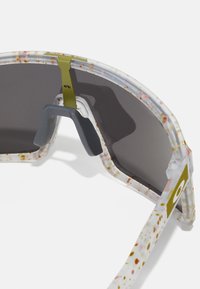 Gafas de sol translúcidas con un patrón moteado en blanco, rosa y verde. Presentan una almohadilla para la nariz gris y lentes oscuros.