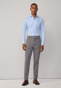 Lichtblauwe lange mouw shirt, grijze op maat gemaakte broek, bruin leren schoenen. Glad stof, getailleerd ontwerp, knoopsluiting kraag, minimale details.