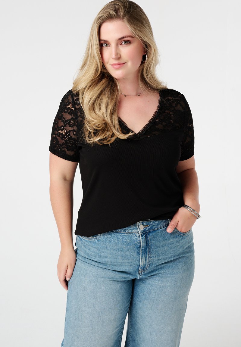 Zwarte top met korte mouwen en kantdetails op de schouders, V-hals en een relaxte pasvorm, gecombineerd met lichtblauwe hoge taille jeans.