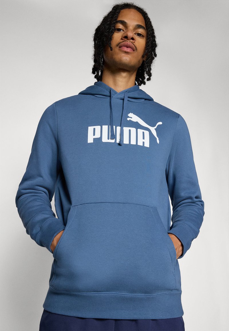 Blauwe hoodie met een groot wit "PUMA" logo en een kleiner logo erboven. Inclusief een voorzak en gestructureerde mouwen. Zacht materiaal.