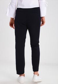 Navyblauwe, slim-fit broek met een zachte textuur, voorzien van een achterzak en omslag onderaan. Gecombineerd met witte sneakers, gezien vanaf de achterkant.