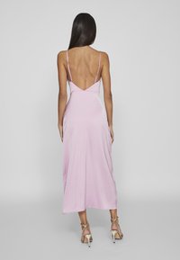 Rosa satin midi-klänning med tunna axelband, djupt ryggdesign och slät textur, kombinerad med beige klackar med remmar.
