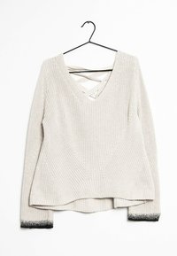 Krämfärgad stickad tröja med långa ärmar, svarta gradientmuddar, V-hals med korsade remmar, hängande på svart galge mot vit bakgrund.