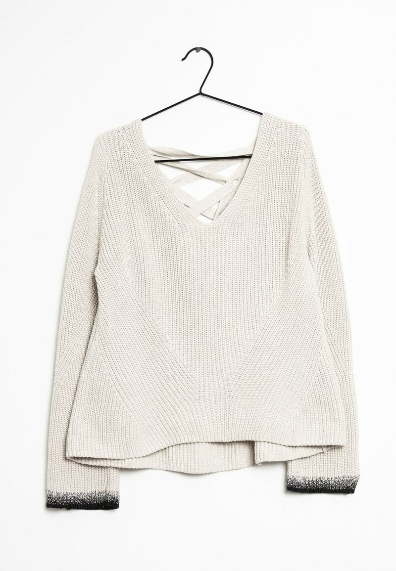 Cremefarvet strikket sweater med lange ærmer, sorte gradientmanchetter, V-udskæring med krydsede stropper, hængende på en sort bøjle mod en hvid baggrund.
