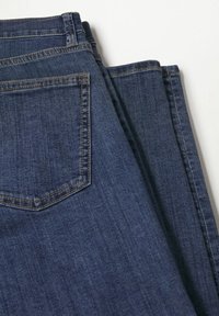 Jeans de mezclilla azul oscuro, doblados con un bolsillo trasero visible y costuras en contraste. Textura suave con un ligero desvanecimiento.