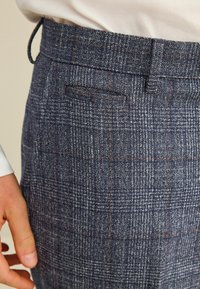 Sötétkék kockás nadrág, texturált anyagból készült, slim fit szabású, övpántokkal és egyetlen hátsó zsebbel, finom kontrasztvarrással.