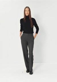 Czarny sweter z golfem oraz szare spodnie garniturowe z prostymi nogawkami, o teksturowanej tkaninie i smukłym kroju. Stylizowane z czarnymi butami.