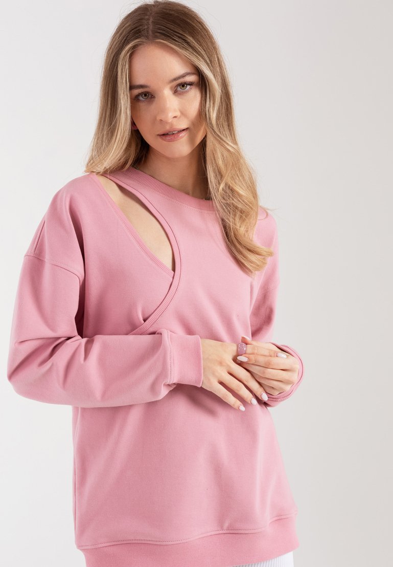 Różowa bluza z unikalnym wycięciem i miękką fakturą. Długie rękawy z prążkowanymi mankietami i luźny krój. Prosty, nowoczesny styl.