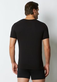 T-shirt nera a maniche corte con una texture liscia e un design aderente, indossata con pantaloni corti neri abbinati, vista da dietro.