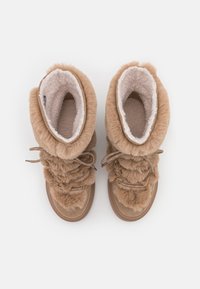 Beige Kunstfell-Stiefel mit plüschigem Innenfutter, gerafftem Design und dekorativen Schnürungen. Die Sohle ist flach und leicht strukturiert für besseren Halt.