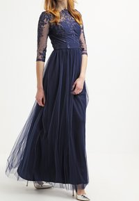 Granatowa maxi sukienka z koronkowymi rękawami o długości trzech ćwiartek, haftowaną górą i tiulową spódnicą. Srebrne szpilki podkreślają całość.