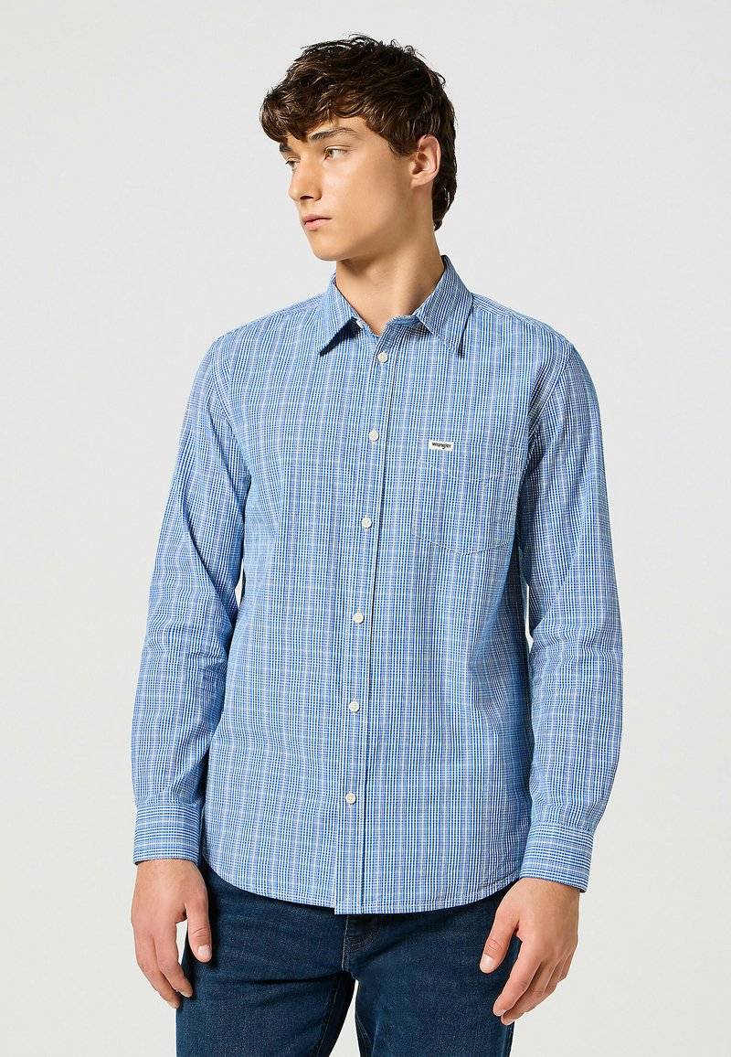 Camisa de manga larga a cuadros azules, hecha de una tela ligera, con cuello abotonado y un bolsillo de parche en el lado izquierdo del pecho.