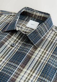 Košeľa na zapínanie s modrým, zeleným a hnedým károvaným vzorom, s golierom, jedným gombíkom pri krku a štruktúrovanou textíliou.