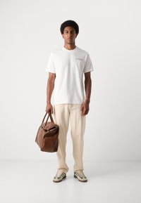 White short-sleeve t-shirt, beige relaxed-fit pants, brown leather bag, and patterned sneakers. Casual outfit with minimal design details.