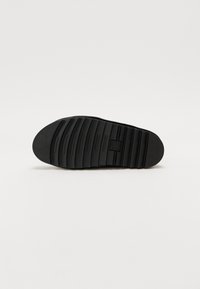 Zwarte rubberen zool met horizontale groeven, ronde neus en textuurgebieden voor grip. Heeft een centrale blindgeperste logo en gladde randen.