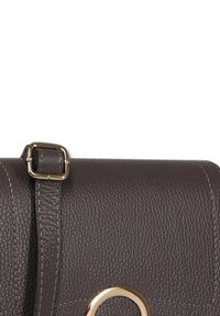 Brown leather handbag with a textured finish, gold hardware, and an adjustable strap. Features a round metal accent on the front.