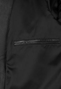 Interior de chaqueta negra con tela lisa, con un detalle de bolsillo con cremallera fino y elegante en el lado izquierdo para un almacenamiento seguro.
