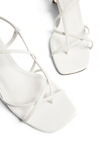 Weiße Sandalen mit Riemchen und quadratischer Zehenpartie. Aus glattem Leder gefertigt, mit verflochtenen Riemen und einem schlanken Absatz.