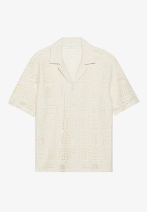 Chemise à manches courtes en tissu crème clair, présentant un design texturé et perforé avec des motifs carrés et un col pointu.