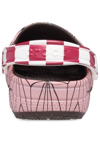 Rosa Crocs mit einem schwarzen Spinnennetzdesign, ausgestattet mit einem weiß-rot gestreiften Riemen. Strukturiertes Fußbett und glatte Außenseite.