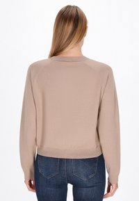 Beige neulepusero, jossa on pyöreä pääntie, pitkät hihat ja ribattu helma. Tasainen tekstuuri, raglanhihaisella muotoilulla, näkyy takaa.