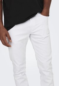 White denim jeans with a slim fit, featuring a five-pocket design and subtle texture. Paired with a black T-shirt.