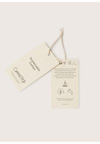 Hållbara bomullsetiketter i ljusbeige återvunnen papper, med tryckt text och ikoner, hållna samman av ett snöre i naturfiber.