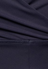 Donkerblauwe rekbare stof met een geplooide textuur, afgewerkt met een gladde afwerking. Zichtbare stiksels langs de onderrand en elastische details aan de bovenkant.