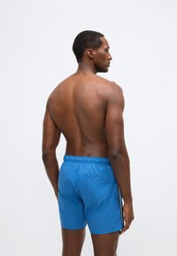 Μπλε μαγιό σορτς με ελαστική μέση, μία πίσω τσέπη και αντίθετες πλευρικές ρίγες. Ελαφρύ ύφασμα, λεία υφή και άνετη εφαρμογή.