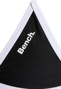 Black fabric bikini top with white accents. Features a triangular shape and “Bench.” logo printed in white on one side.