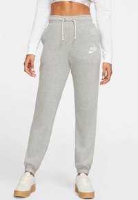 Šedé tepláky s elastickými manžetami, stahovací šňůrkou v pase a bílým logem Nike na levém stehně. Doplněné bílými teniskami.