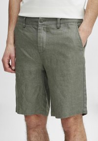 Grå linshorts med rett snitt, har to sidelommer og knappelukking. Stoffets tekstur virker lett og litt rynket.