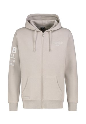 Lichtbeige ritsjack van zacht materiaal, met een capuchon met trekkoord, twee voorkruiszakken en witte bedrukte tekst op de linker mouw.