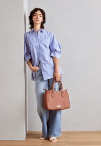 Tan leren handtas met een gestructureerde vorm en dubbele handvatten. Blauwe en witte gestreepte, knoopsluiting shirt met mouwen die bij de manchetten zijn gathered. Lichtblauwe jeans.