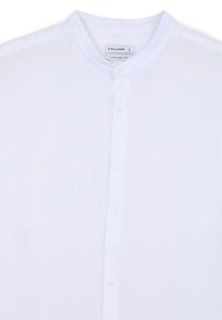 Camicia bianca in cotone con colletto alla coreana, dotata di bottoni sulla parte anteriore e una finitura leggermente strutturata. L'etichetta riporta "CALLIOPE" e taglia "L".