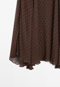 Brown skirt made of lightweight, sheer fabric with black polka dots. Features a wavy hemline and layered design for added movement.