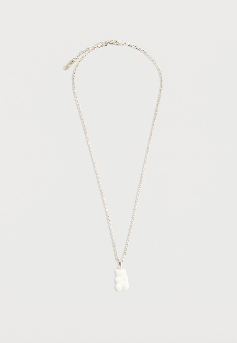 Ασημένιο κολιέ με αλυσίδα και μικρό μενταγιόν σε σχήμα λευκής καραμέλας αρκουδάκι σε λευκό φόντο.