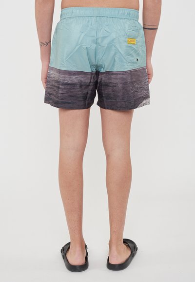 Costume da bagno azzurro chiaro con un motivo orizzontale sfumato in nero, vita elastica e una tasca sul retro con un'etichetta gialla.