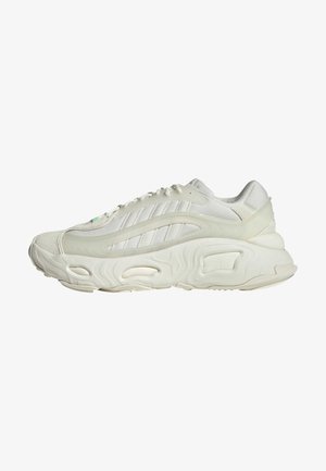 Biały sportowy sneaker z teksturowaną, grubą podeszwą i subtelnymi paskami po boku, widziany z lewej strony na jednolitym białym tle.